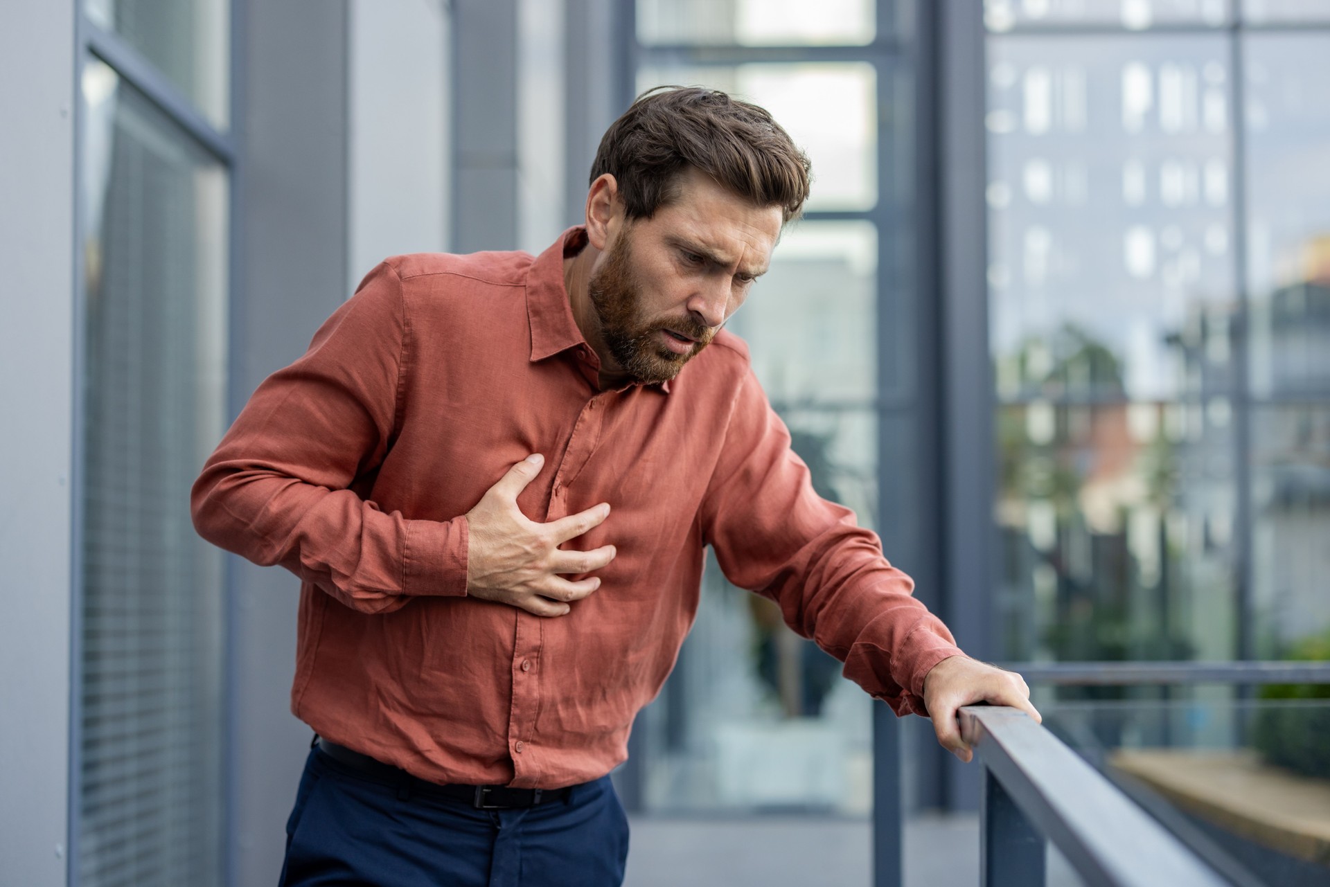 Mature businessman experiencing chest discomfort outside modern urban office building