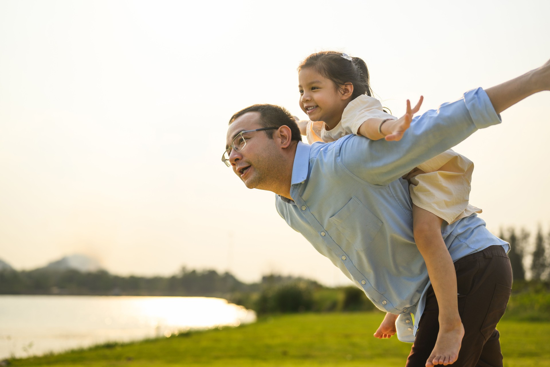 Happy father holding daughter on back playing together in garden
